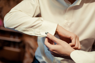 Obraz na płótnie Canvas The groom fastens the cufflink on the shirt sleeve close-up