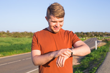 Male runner jogging outside looking at his wearable fitness tracker outside.
