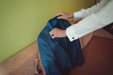 Elegant groom in wedding jacket wearing white shirt and turquoise tie. Groom's hands on blue suit.