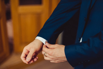 Elegant groom in wedding jacket wearing white shirt and turquoise tie. Groom's hands on blue suit.