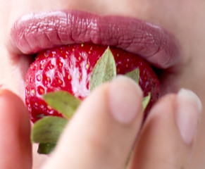 Woman lips with red strawberry on blur background. Pink lipstick. Fresh berry. Girl eating strawberry.