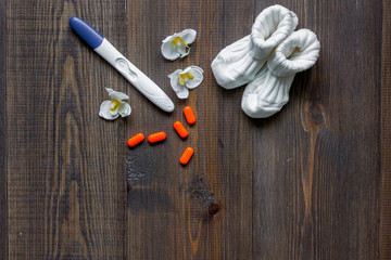 Pregnancy planning. Contraceptive pills, pregnancy test and booties on wooden background top view copyspace