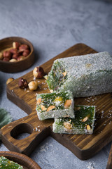Turkish green delight with nuts on wooden brown board and plate standing on grey concrete background. Still life
