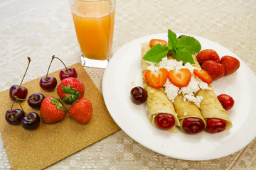 Dessert of pancakes stuffed with cottage cheese with strawberries and cherries, orange juice is on the table. horizontal