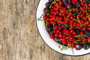 Fresh colorful berries in bowl on rustic wooden table