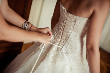 Fashionable bridesmaids dresses helped wear bow on back of wedding dress bride. Morning wedding day.