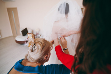 Fashionable bridesmaids dresses helped wear bow on back of wedding dress bride. Morning wedding day.