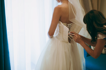 Fashionable bridesmaids dresses helped wear bow on back of wedding dress bride. Morning wedding day.