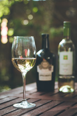 Weinglas mit Weißwein, Weinflaschen, Gastgarten in der Abendsonne
