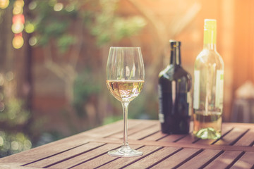 Weinglas mit Weißwein, Weinflaschen, Gastgarten in der Abendsonne