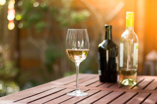 Weinglas mit Weißwein, Weinflaschen, Gastgarten in der Abendsonne