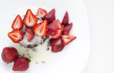 Delicious homemade chocolate cake with fresh red strawberries and cream sauce on white plate.