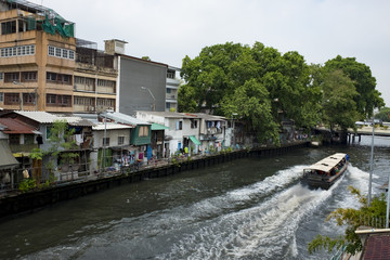 BANGKOK, THAILAND. Passenger boat running across a canal bridge at Phasi-Charoen Canal with community background