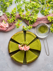 Matcha baked cheese cake and pink flowers on gray concrete background