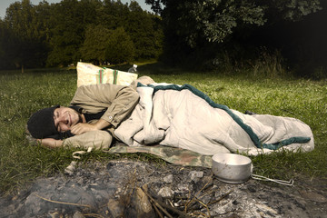 Vagabond young man sleeping in park near fireplace
