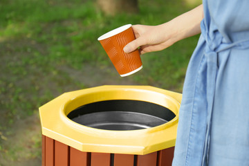 Young woman throwing plastic cup in litter bin outdoors, closeup