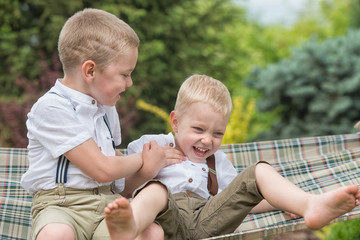 The two brothers are resting and having fun .Children ride in a hammock.	