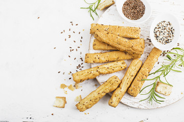 Bread sticks from puff pastry with flax and sesame seeds on a light background with rosemary. Top...