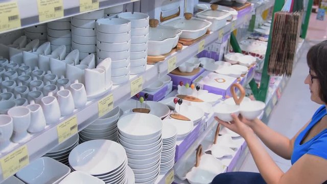 Young woman looking over white dishes in the store. Shopping for home goods in the hypermarket