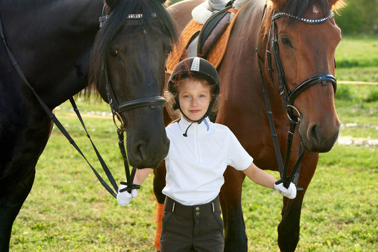 Pretty little girl jockey communicating with her horses in professional outfit