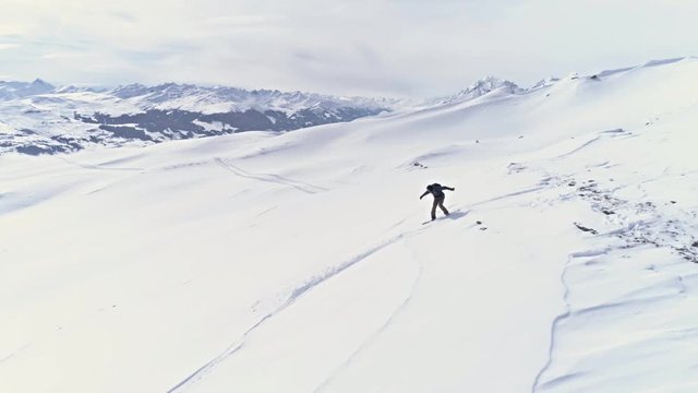 Aerial footage of a snowboarder going down the backcountry in a winter resort in Switzerland. Drone footage in slowmotion in 4k quality.