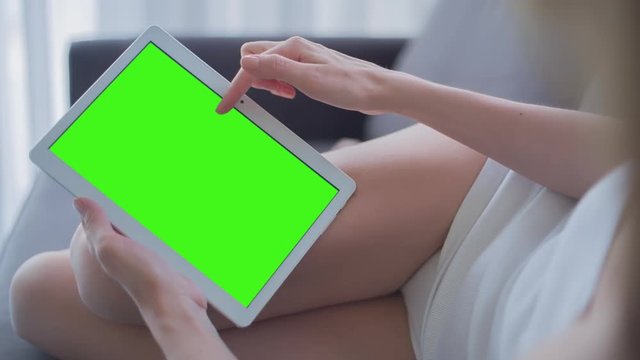 Young Woman in white top laying on couch uses Tablet PC with pre-keyed green screen. Few types of gestures - scrolling up and down, tapping, zoom in and out. Perfect for screen compositing