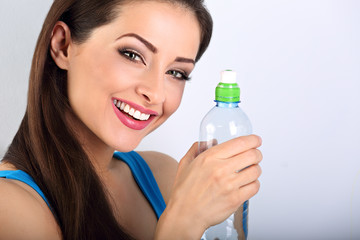 Beautiful happy toothy smiling makeup woman holding and drinking water from the bottle. Closeup portrait on blue background