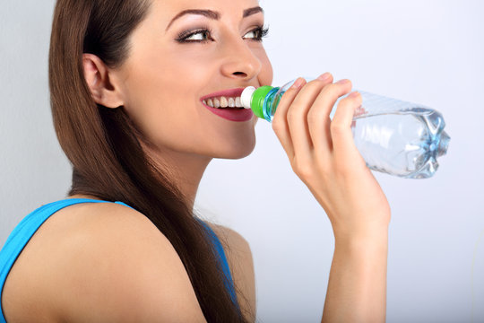 Beautiful happy toothy smiling makeup woman drinking water from the bottle. Healthy face skin. Closeup portrait.