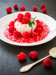 Panna cotta with raspberries syrup in a plate on a dark background, traditional italian tasty dessert.