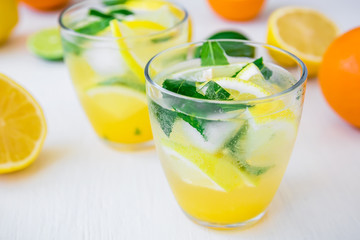 Fresh citrus lemonade with limes and lemons in glasses on white table