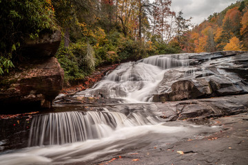 Fototapeta premium beautiful waterfall over three steps with forest in fall colors in the background