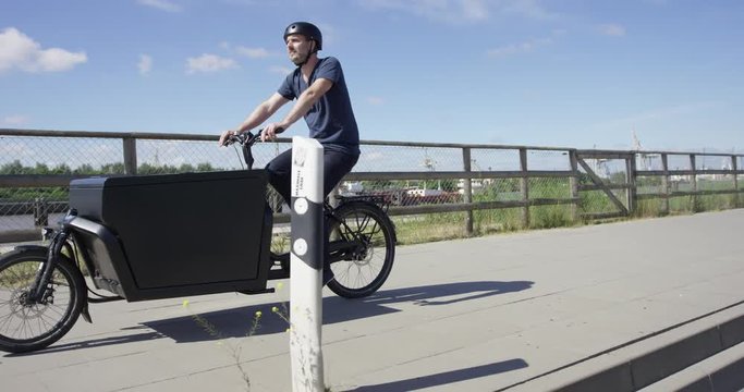 Handsome man riding on black cargo bicycle along a river
