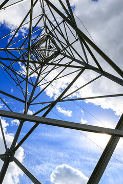 The electricity transmission pylon in daytime outdoors. Electricity tower standard overhead power line transmission tower on the background blue sky and white cloud. 