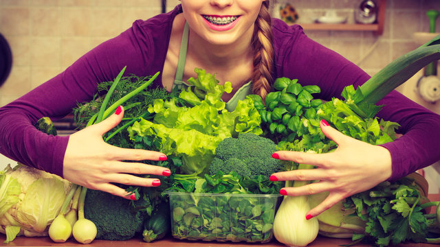 Smiling woman in kitchen with green vegetables