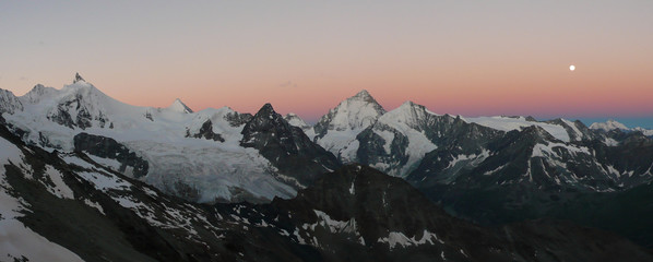 dawn and early morning over the Swiss Alps in the Valais with the Zinalrothorn and a full moon in a pink sky