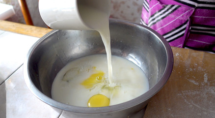 Preparation for kneading the dough. The basis of the dough. Pouring milk into a metal bowl with eggs