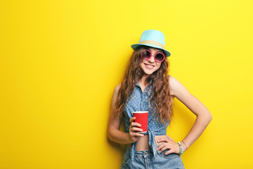 Portrait of young woman with hat, sunglasses and red cup on yellow background