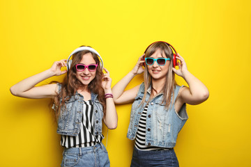 Portrait of two young woman with sunglasses and headphones on yellow background
