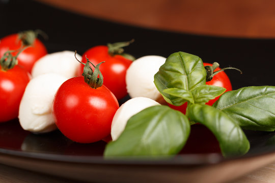 Tomaten und Mini Mozzarella auf schwarzem Teller mit Basilikum