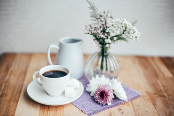 Obraz na płótnie Canvas Freshly brewed cup of american coffee with two cubes of sugar in white porcelain china cup, decorated with flowers and placed on wooden cutting board