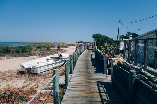 Wooden deck and walk goes into distance on empty beach, with abandoned old fishing motorboats and little huts, hot summer day, unconventional travel destination for nomads