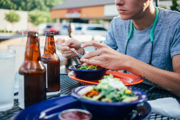 Man on a date in restaurant eats a bowl of fresh vegetables rice and shrimps, served with cold beer bottles, delicious, healthy and tasty dinner