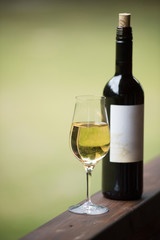 A glass with a white wine and the black wine bottle with label. Selective focus.