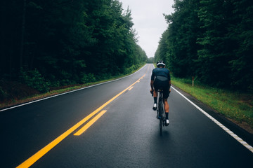 Selective focus shot of professional road cyclist riding down wet and windy mountain road in forest, on aero road bike from carbon