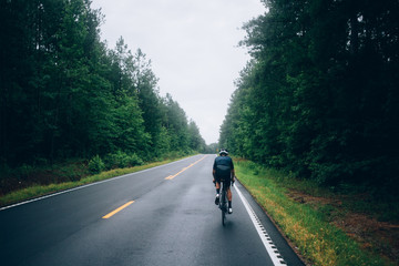 Fototapeta premium Selective focus shot of professional road cyclist riding down wet and windy mountain road in forest, on aero road bike from carbon