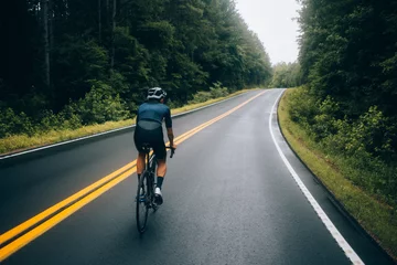  Selectieve focus van professionele wielrenner die over een natte en winderige bergweg in het bos rijdt, op een aero-racefiets van carbon © BublikHaus