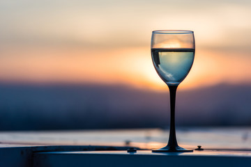 A glass with a white wine in the light of the setting sun. Vibrant alcohol background.