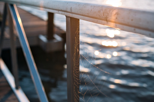 Spider web hanging on lake river boat deck or dock with morning dew or rain
