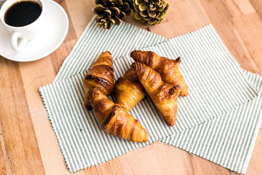 Top view of crispy french tasty butter croissants beautifully assembled on wooden cutting board with lot of flavour and white cup of black coffee in cafe or restaurant