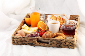 breakfast in bed with fruits and pastries on a tray -waffles, croissants, coffe and juice